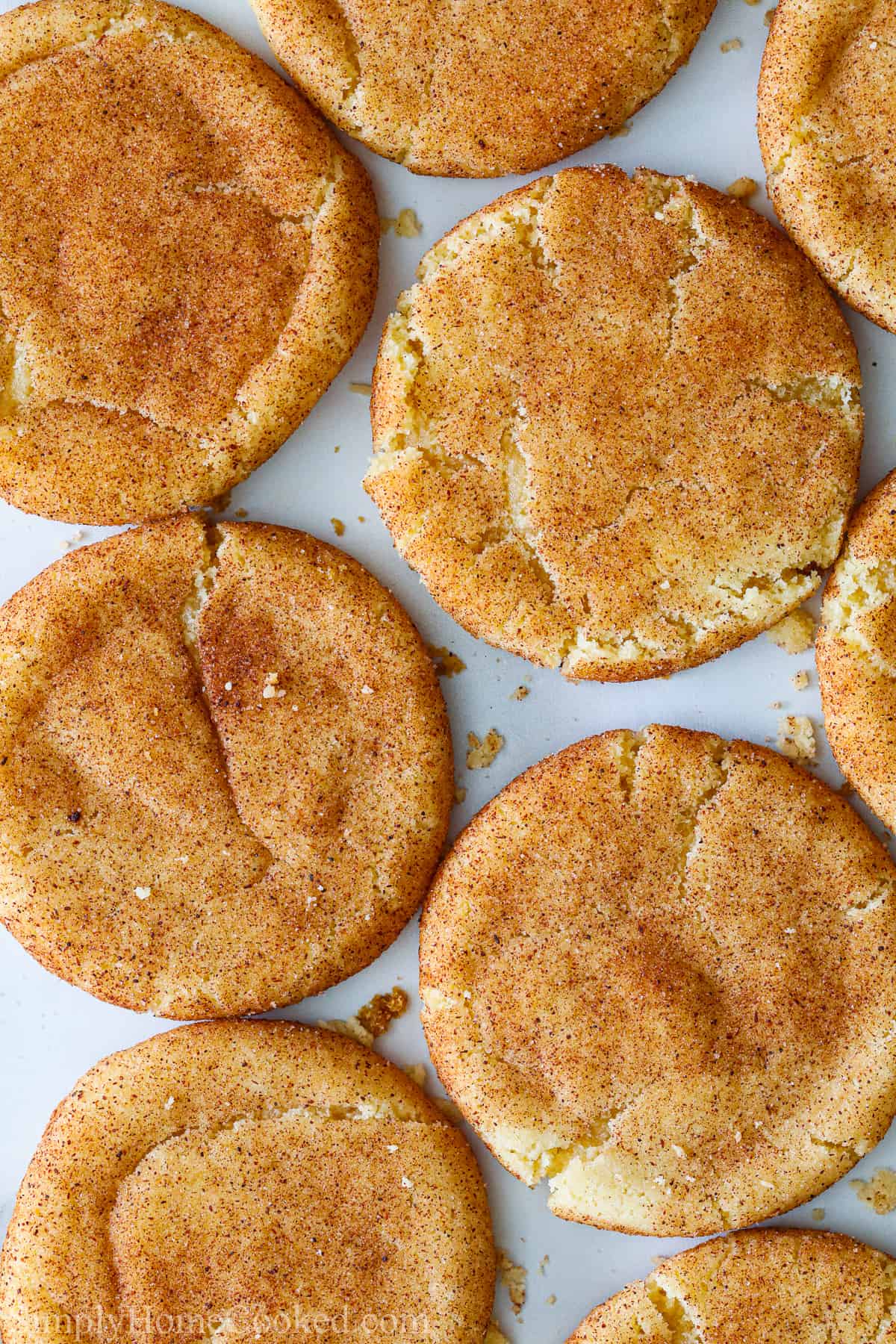These Soft Snickerdoodle Cookies are chewy, sweet, and have a delicious coating of cinnamon-sugar on top. You'll love the taste and texture of these cookies. #cinnamonsugarsnickerdoodles #favoritesnickerdoodlerecipe #snickerdoodlesoftcookierecipe #bestrecipesnickerdoodles Soft Snickerdoodle Cookies spread out on a baking sheet.