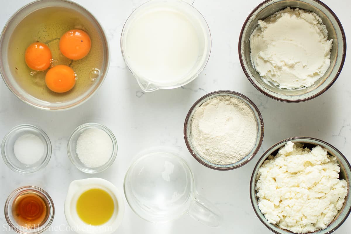 Ingredients for Cheese Blintz, including eggs, sugar, flour, vanilla, olive oil, milk, water, cream cheese, cottage cheese, and salt on a white background.