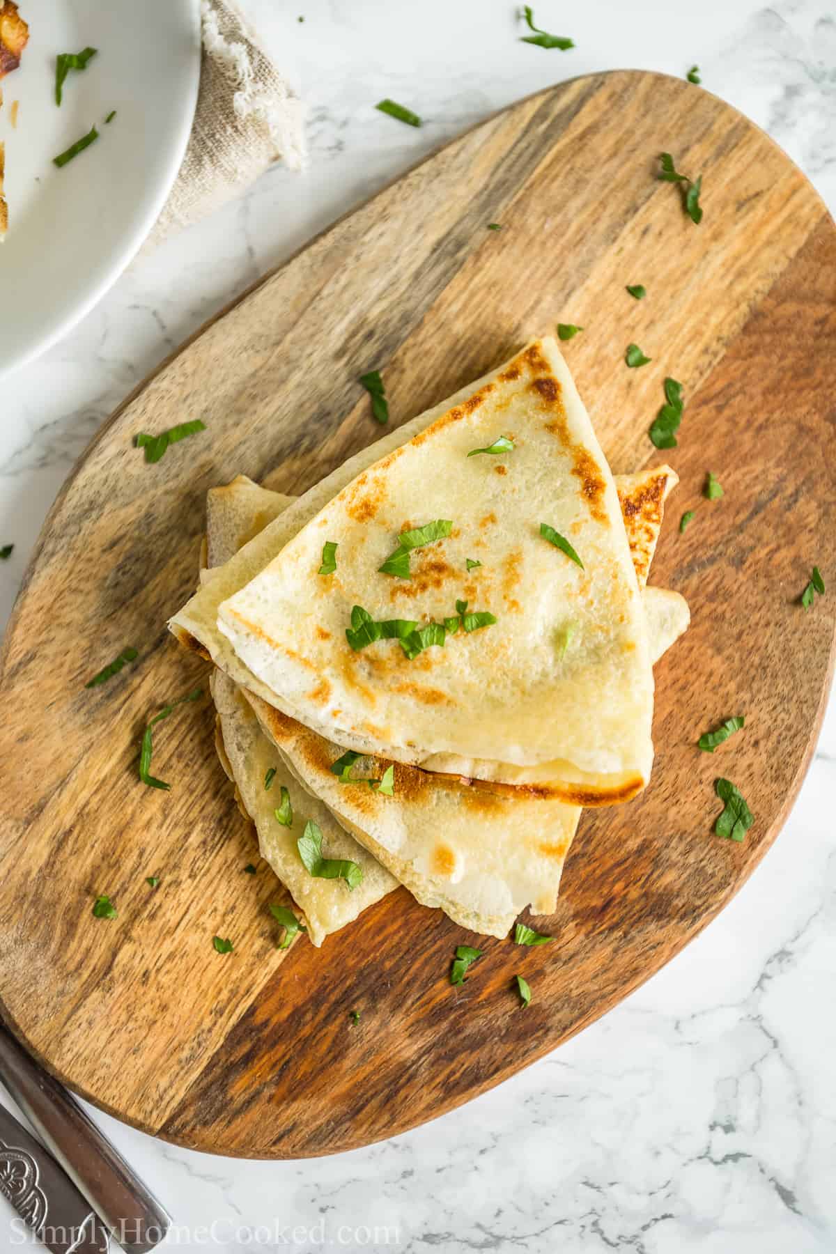 Close up of Savory Crepes with Chicken and Mushroom Filling stacked on a wooden board with garnish sprinkled on top.