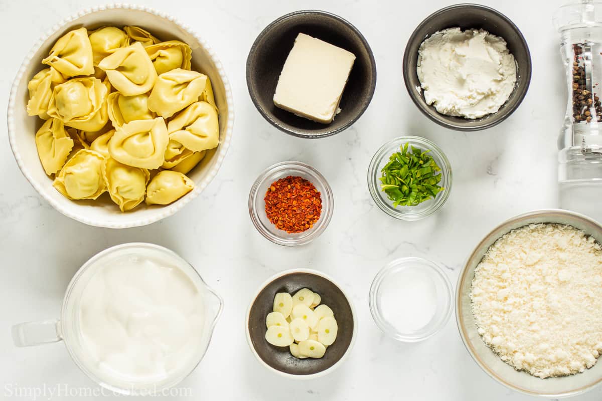 Ingredients for Creamy Tortellini Alfredo, including cheese tortellini, heavy cream, cream cheese, butter, garlic, Parmesan, salt, pepper, red pepper flakes, and parsley on a white background.