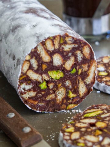 A stick of chocolate salami with a slice of it sliced of and a knife beside it.