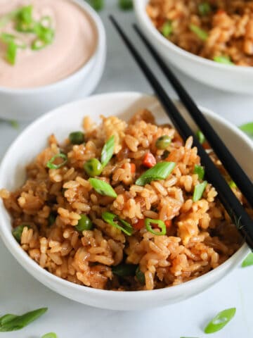 Bowl of Hibachi Fried Rice with chopsticks on the side and another bowl in the background with some yum yum sauce.