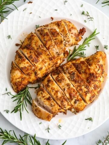 Close up of Juicy Air Fryer Chicken Breast on a white plate with rosemary garnish.