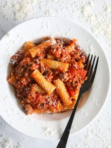 Plate of Rigatoni Bolognese with a fork and grated Parmesan cheese.
