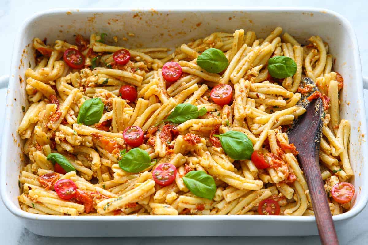 Baking dish with Baked Feta Pasta mixed with a wooden spoon