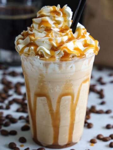 Caramel Frappuccino with a whipped cream and caramel sauce and a straw.