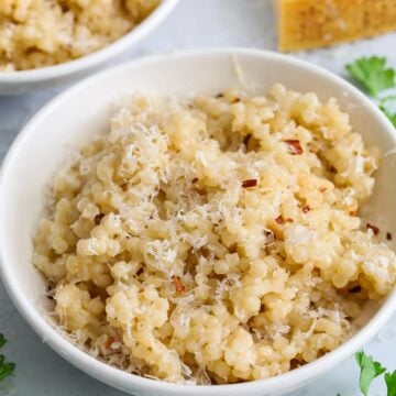 close up image of cooked couscous in a white bowl with red pepper flakes on top