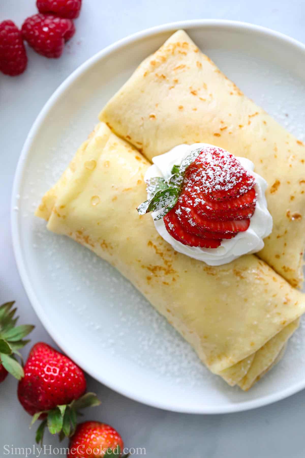 Overview of folded crepes with whipped cream and strawberries