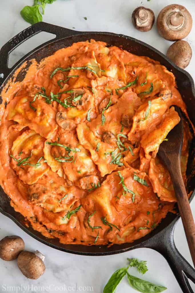 overhead image of sausage ravioli in a cast iron pan with a wooden spoon inisde.