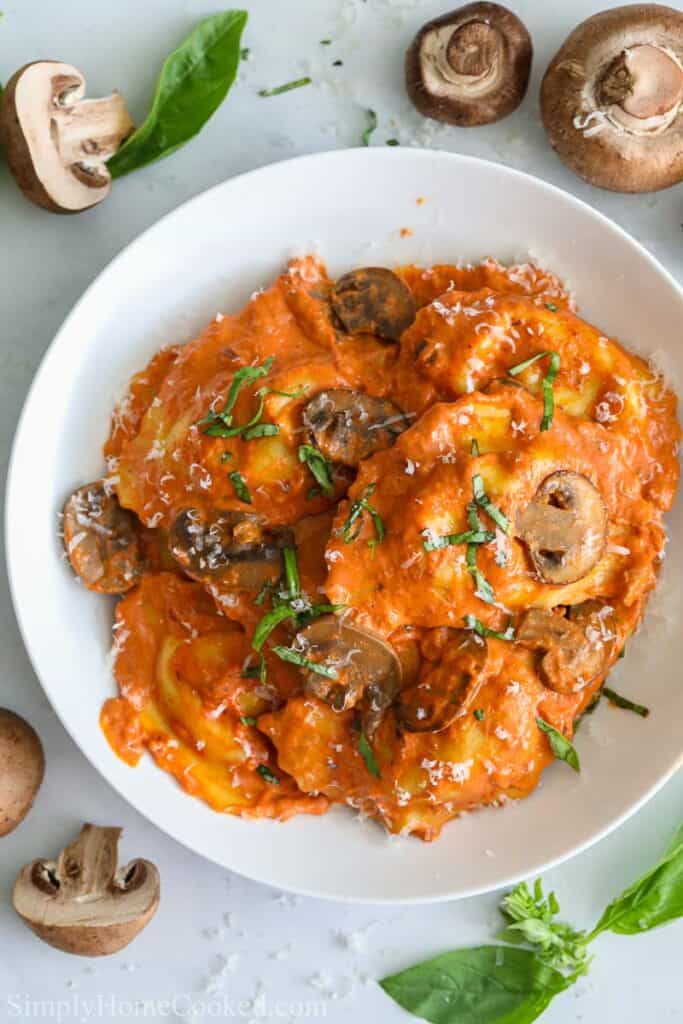overhead image of sausage ravioli in a white dish with mushroom and basil on top
