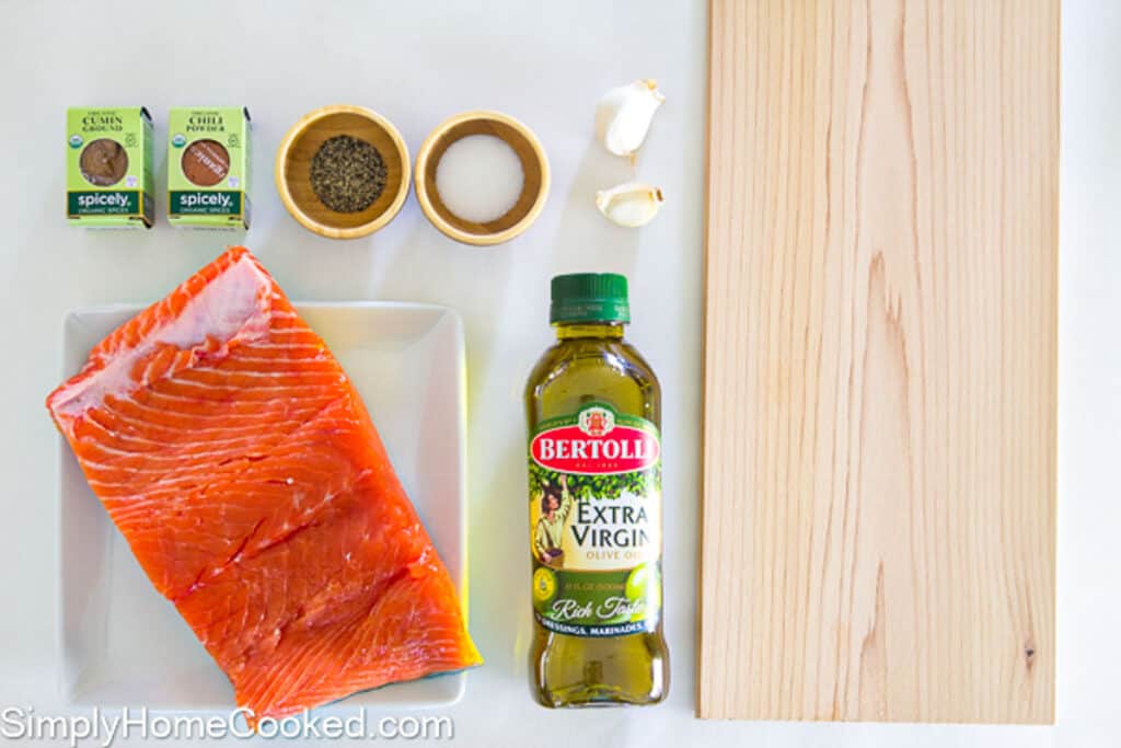 Ingredients for Cedar Plank Salmon, including salmon, cedar planks, olive oil, salt, pepper, garlic cloves, cumin, and chili powder.