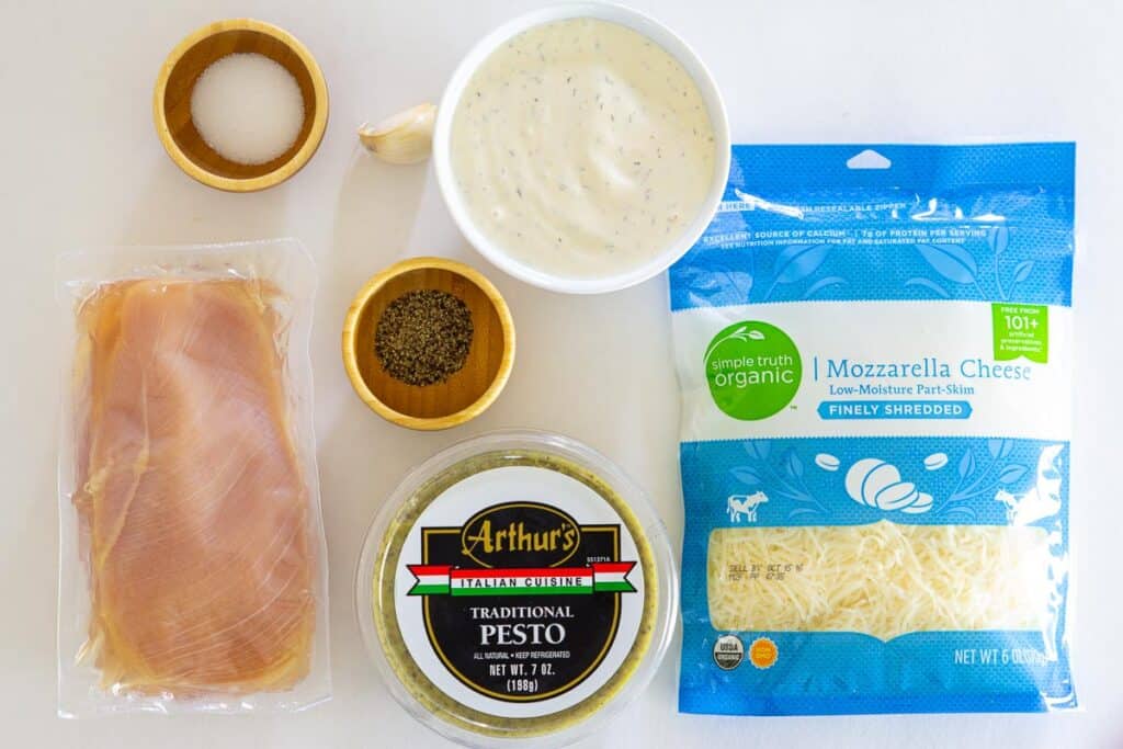 Ingredients for Chicken Pesto Pizza, including chicken breast, salt, pepper, garlic clove, ranch dressing, pesto, and mozzarella cheese.