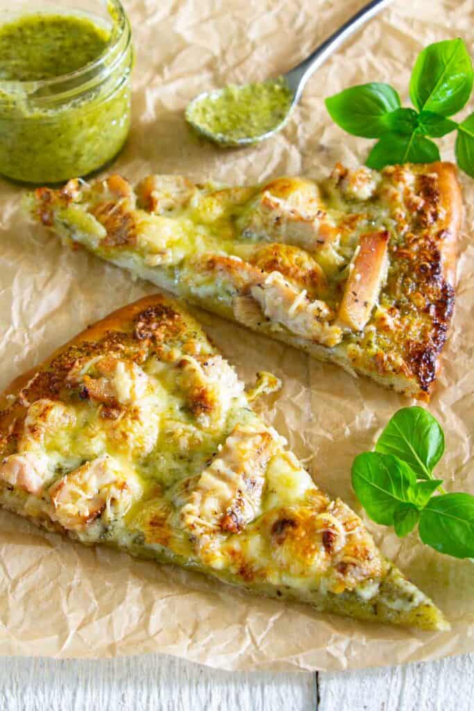 Chicken Pesto Pizza combines all of your favorite flavors into a convenient easy to eat pizza recipe that is elegant and delicious while being favorite comfort food. #pestopizza #pizzarecipe #summerpizza #grilledpizza #chickenpizza #whitesaucepizza Slices of Chicken Pesto Pizza with pesto and basil nearby