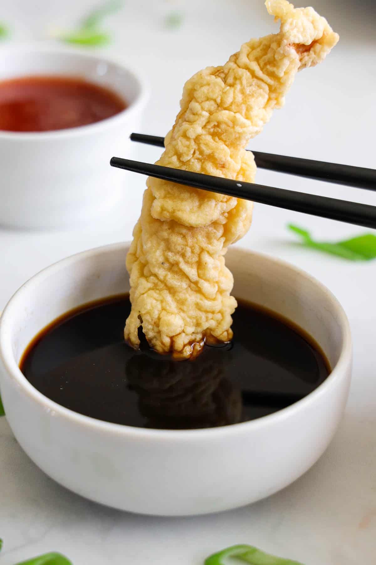 Close up of Chicken Tempura being dipped into sauce with chopsticks.