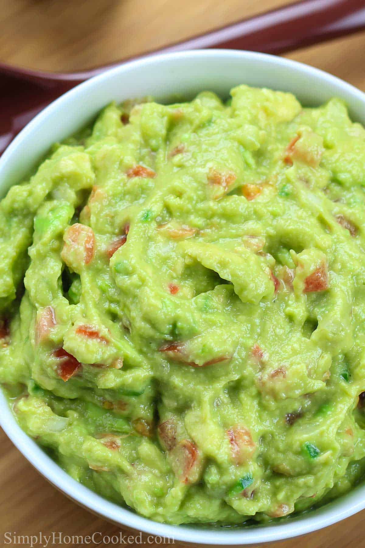 This Easy Authentic Guacamole recipe will ruin you for store-bought guac. It's smooth and creamy with chunks of tomato and a hint of garlic and lime - absolutely delicious! #easyguacamole #authenticguacamole #guacamolerecipe #easyauthenticguacamole Overhead view of Guacamole in a white bowl