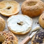 Sourdough bagels with different toppings, one spread with cream cheese, and a knife.