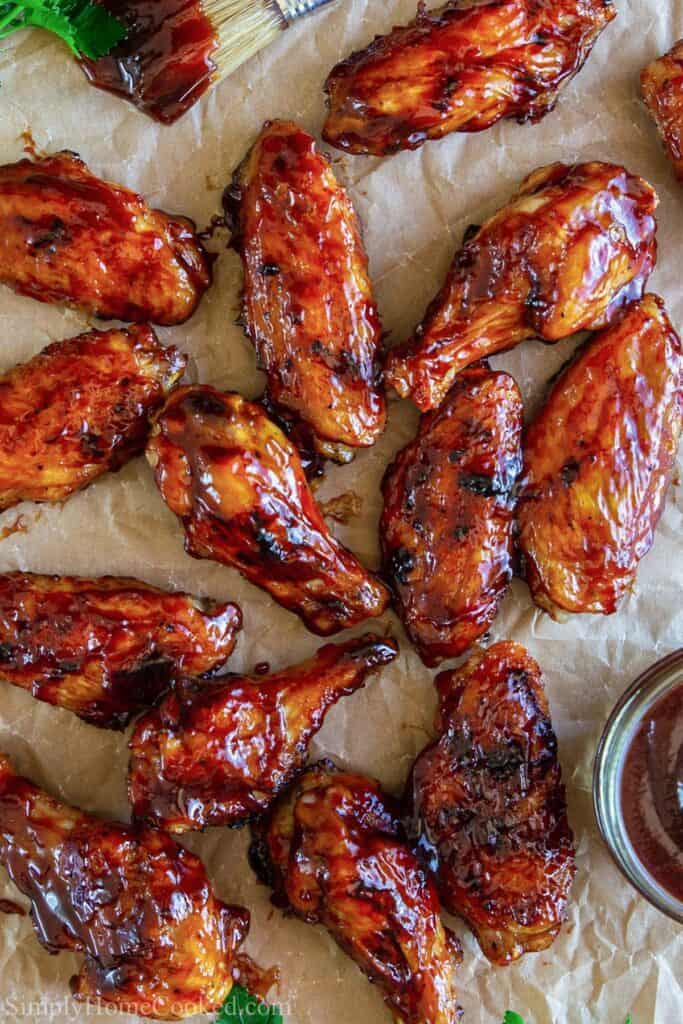 This Delicious grilled BBQ wings recipe is a classic appetizer! Made with an easy 4 ingredient homemade bbq sauce. Quick, easy, and downright delicious. #barbecuewings #bbqwings #chickenwings #grilledwings #easychickickenwings overhead image of grilled bbq chicken wings on a sheet of brown parchment paper