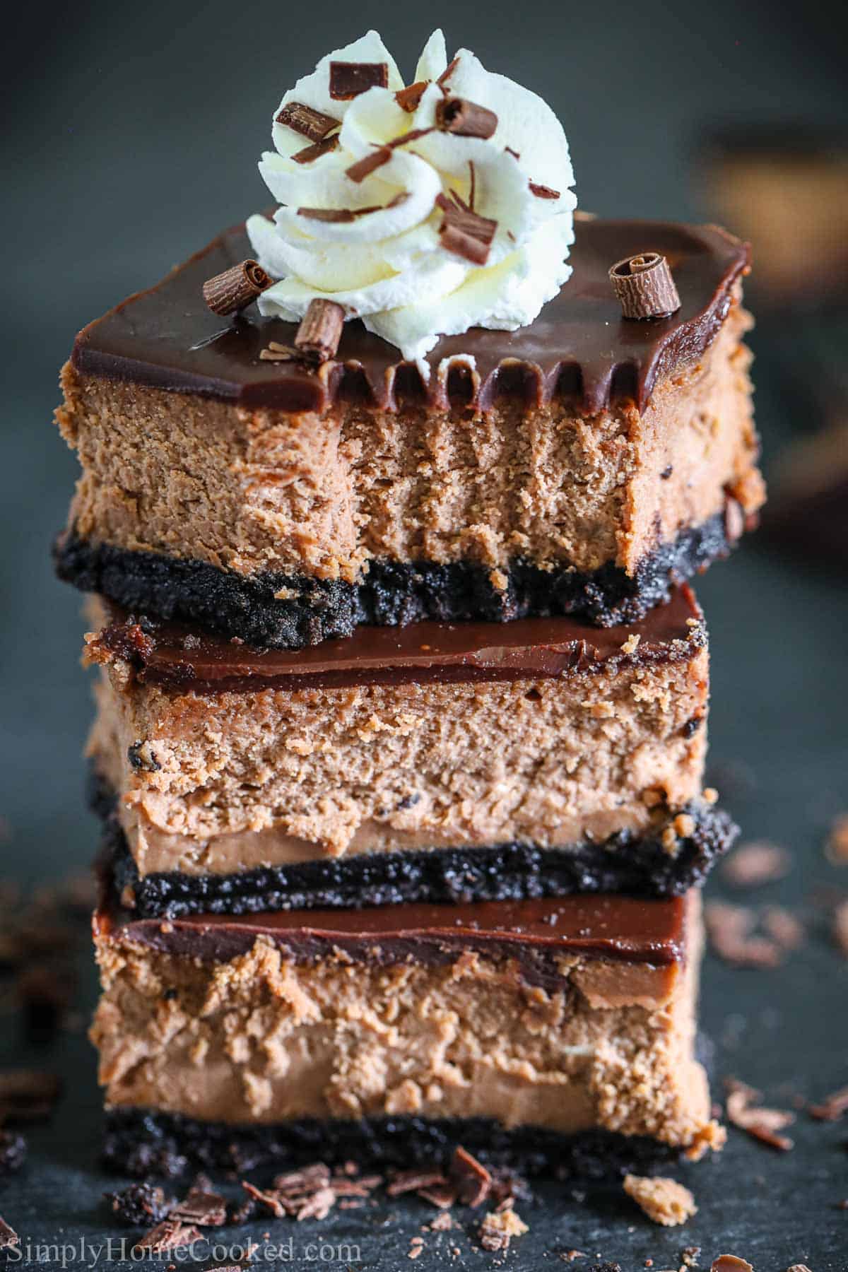 These Chocolate Cheesecake Bars are to die for. Decadent and rich and oh so chocolaty, they are easy to make and taste delicious. #easychocolatecheesecakebars #easyhomemadecgeesecakerecipe #richchocolatecheesecake #bestchocolatecheesecakerecipe Stack of Chocolate Cheese Cake Bars with whipped cream on top