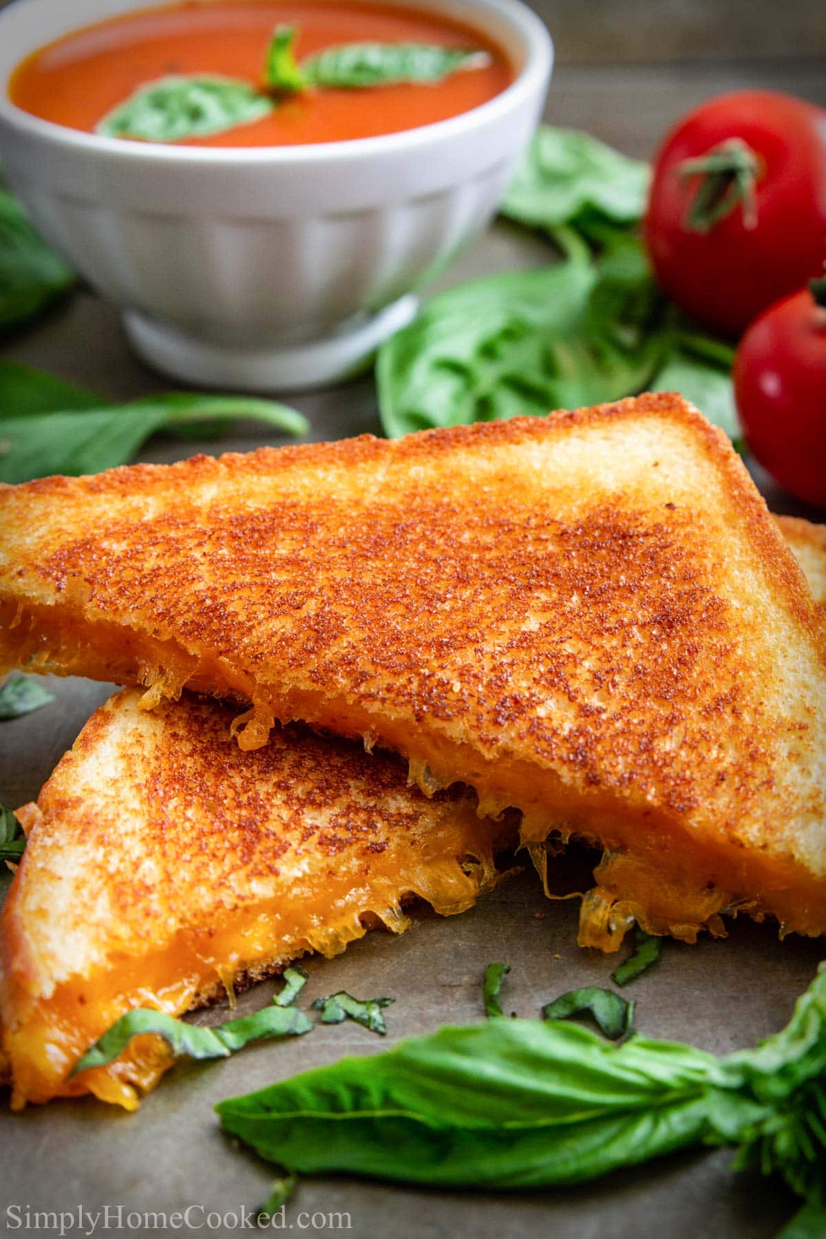 Grilled Cheese Sandwich cut in half with tomato soup in the background.