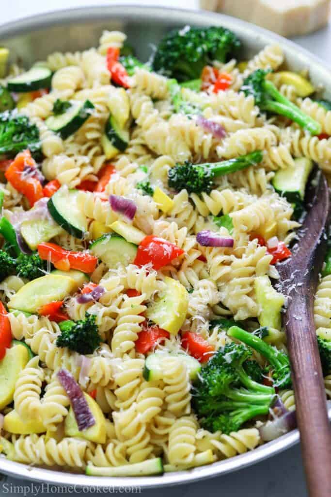 This Easy Pasta Primavera is a delicious vegetarian dish that is full of flavor. Melted Parmesan and lots of fresh vegetables make for a tasty pasta dinner. #easypastaprimaverarecipe #homemadeeasypastaprimavera #homemadepastaprimavera #vegetarianpasta Vertical image of Pasta Primavera in a pan with a wooden spoon