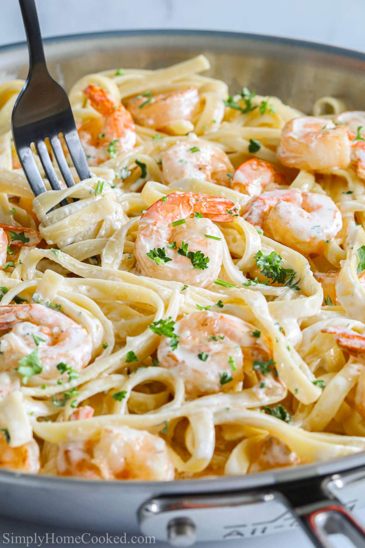This Shrimp Alfredo Pasta is so deliciously rich. Made with garlic, cream, and Parmesan, you'll love this homemade Italian favorite. #Italianfood #pastaalfredo #shrimppastaalfredo #alfredosaucerecipe Vertical image of Shrimp Alfredo Pasta in a pan with a fork