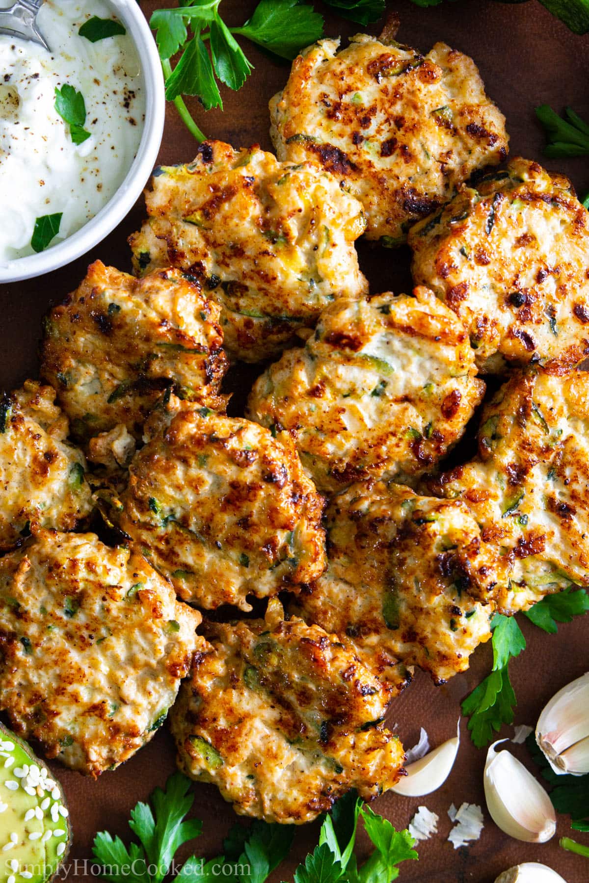 These paleo chicken zucchini fritters are protein packed, antioxidant rich, and super flavorful. This recipe is also whole 30, gluten free, and keto. #zucchinifritters #chickenfritters #whole30chicken #paleochicken #easychicken #quickchicken Vertical image of Chicken Fritters with Zucchini with sauce nearby