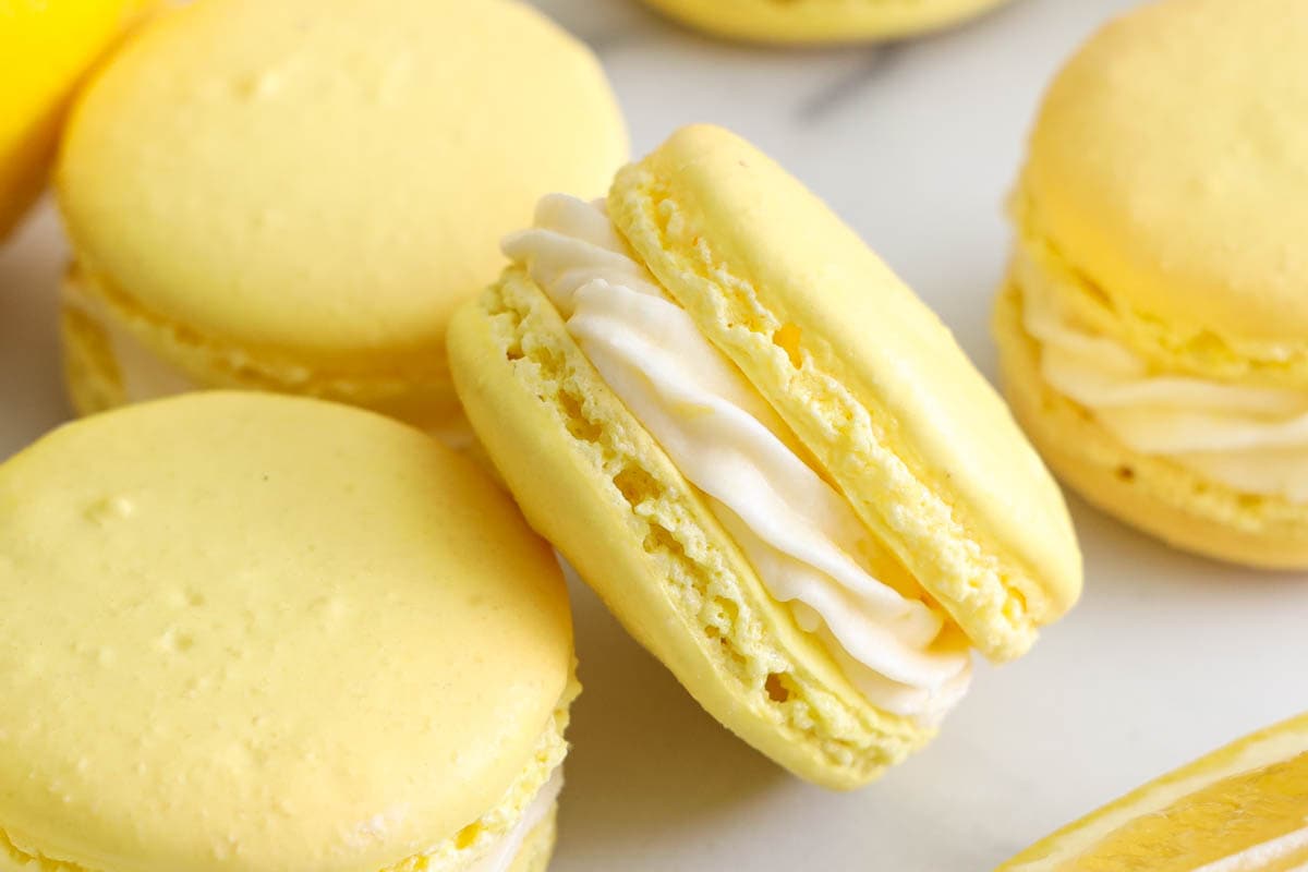 Lemon curd and buttercream filled Lemon Macarons resting near a lemon