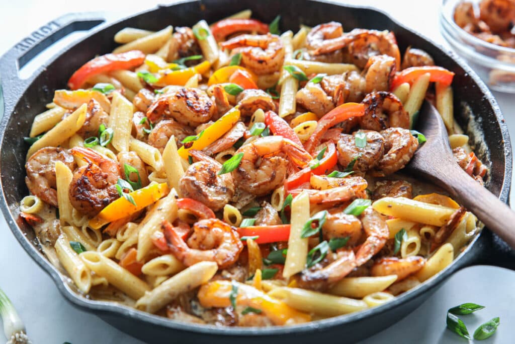 horizontal image of shrimp rasta in a cast iron pan with a wooden spoon inside