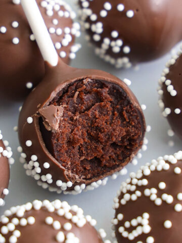 Closeup of a Chocolate Cake Pop with nonpareils, one with a bite missing.