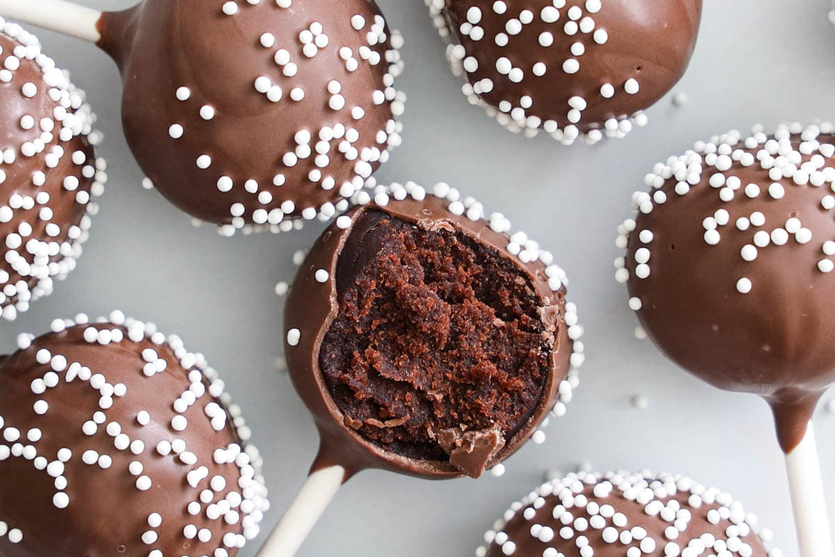 horizontal image of Chocolate cake pops covered in nonpareils, one with a bite missing.