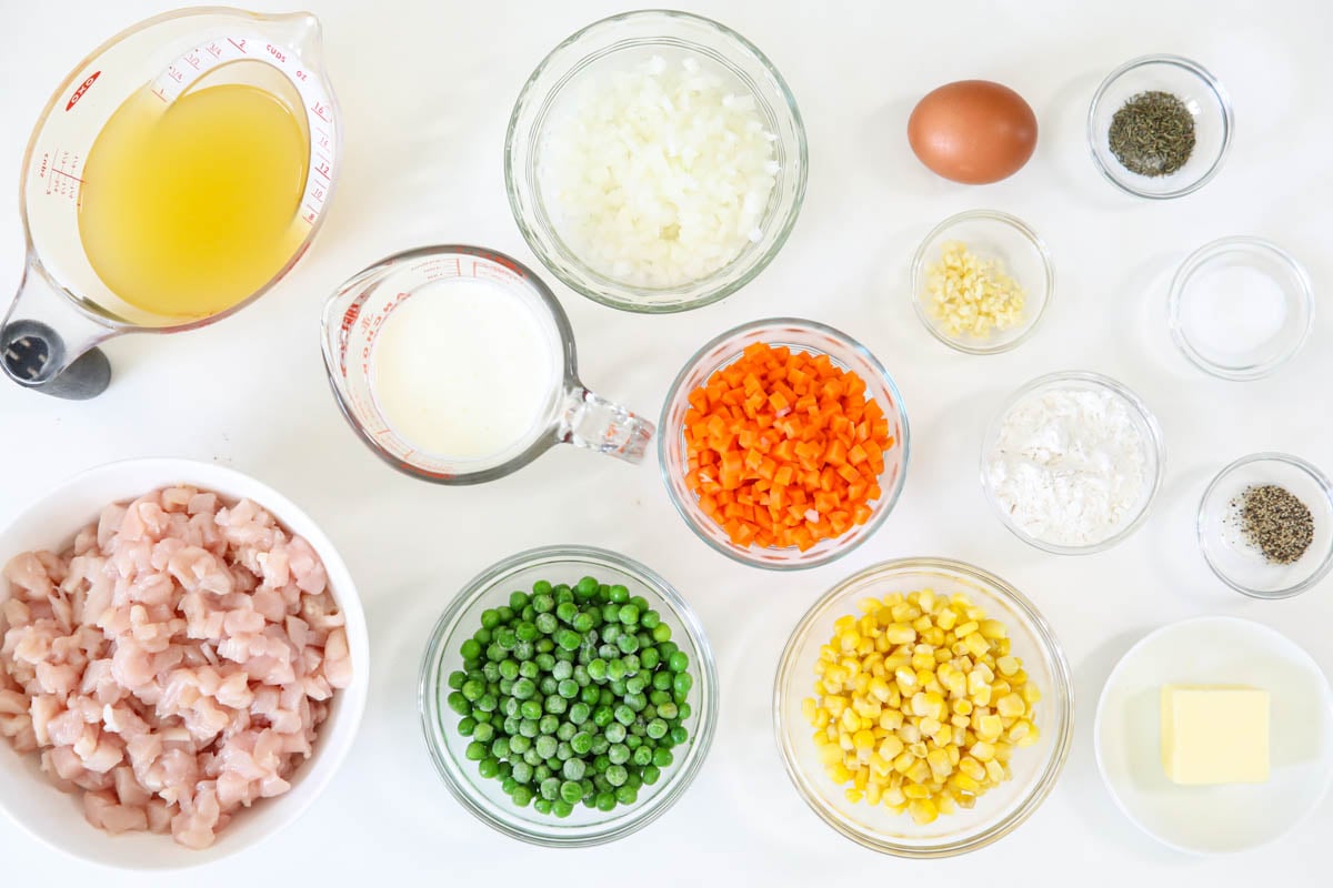 Ingredients for Mini Chicken Pot Pies, including chicken, broth, peas, corn, carrots, onion, garlic, flour, cream, egg, salt, pepper, butter, and thyme.