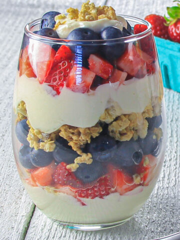 Vertical image of a Yogurt Parfait in a glass, with strawberries in the background.