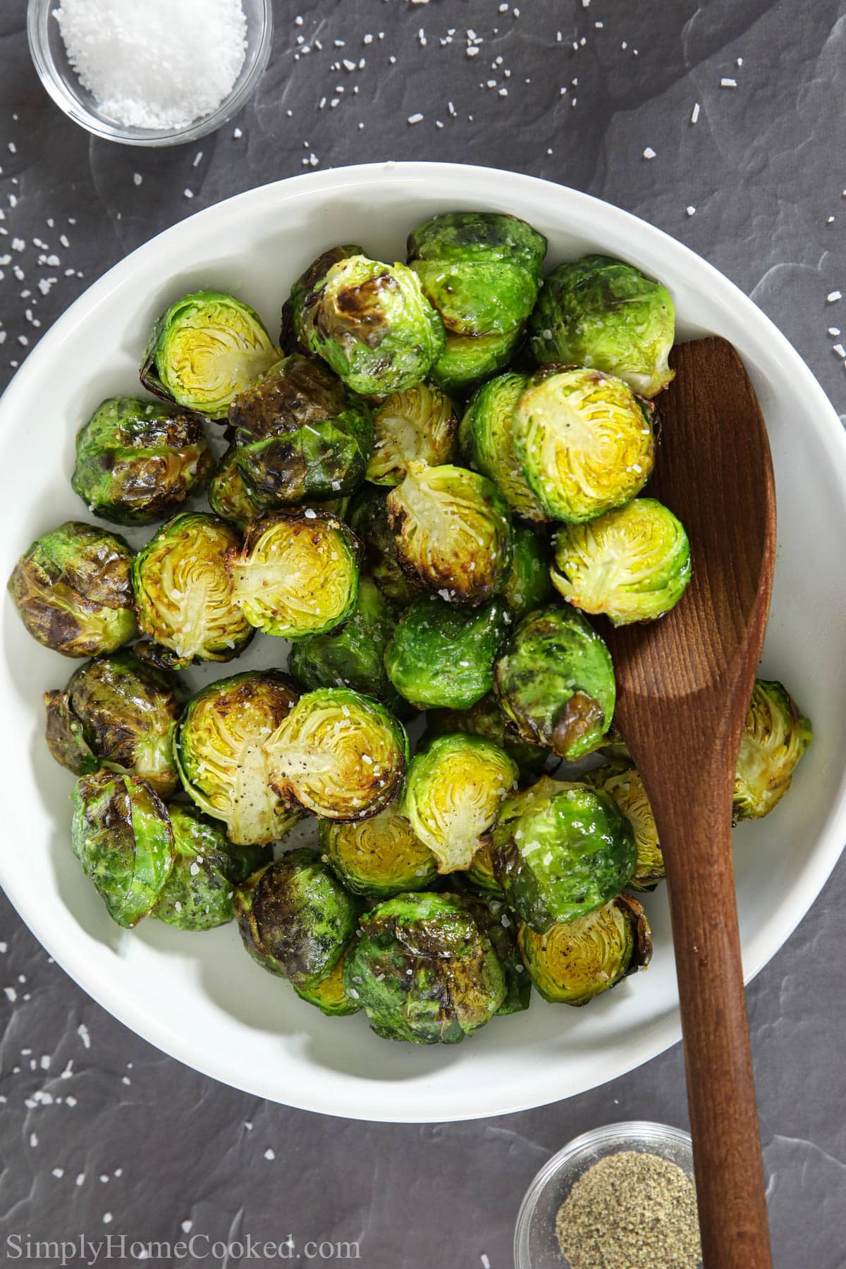 Vertical image of Air Fryer Brussels Sprouts in a bowl with a wooden spoon.