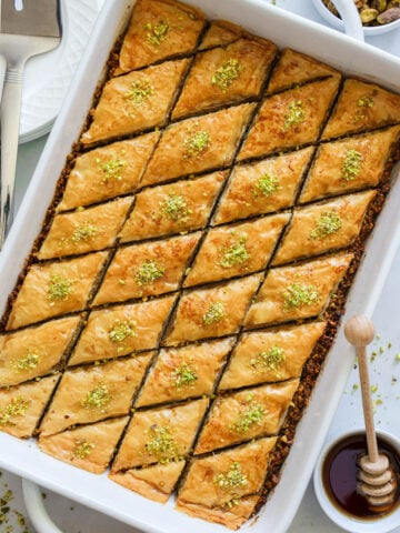 Vertical image of Baklava in a baking pan with honey on the side.