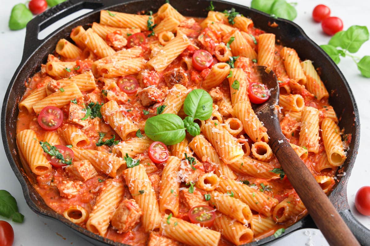 Pan of Chicken Riggies with a wooden spoon in it and basil on top.