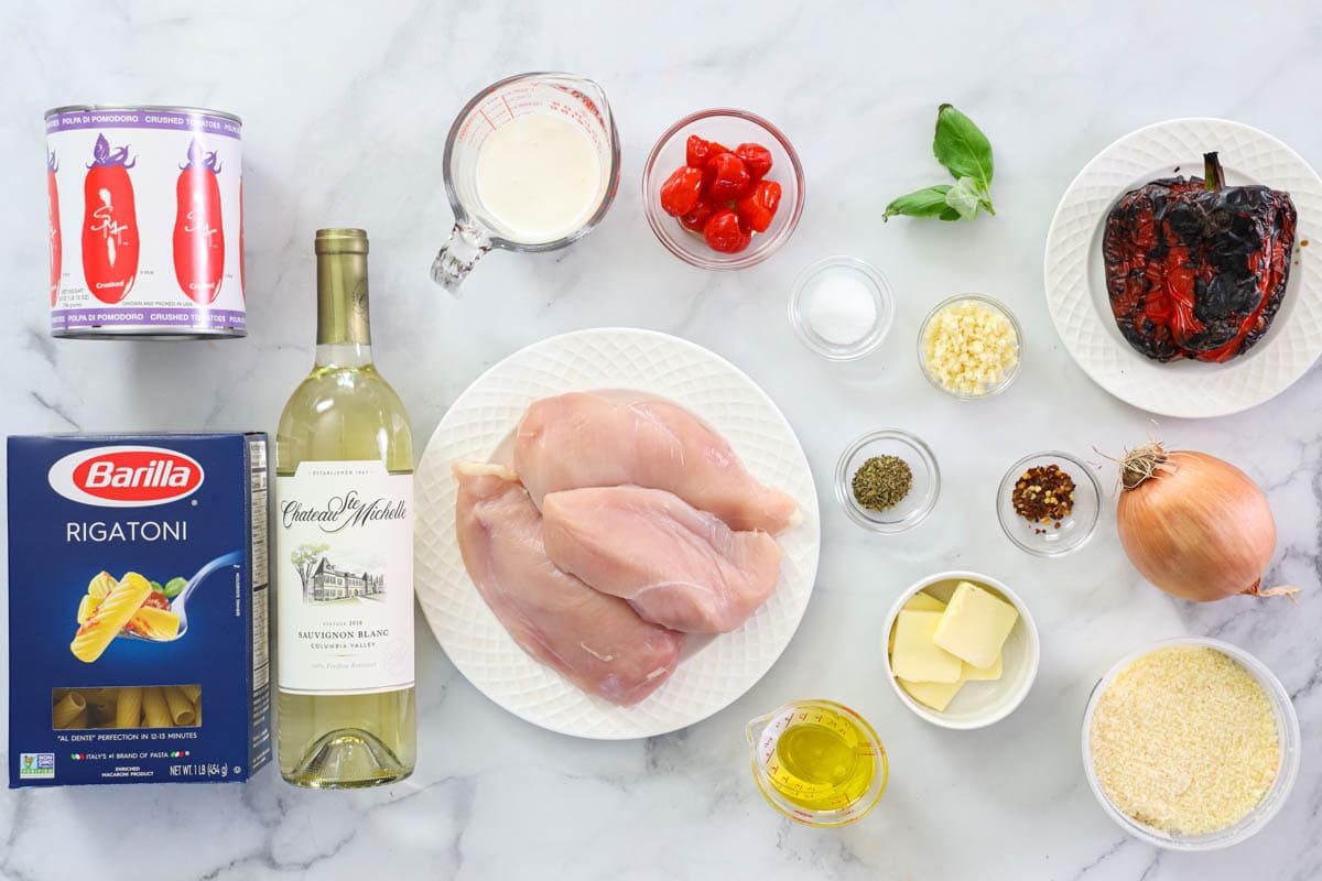 Ingredients for Chicken Riggies, including rigatoni pasta, crushed tomatoes, chicken breast, white wine, heavy cream, hot cherry tomatoes, basil, roasted bell pepper, minced garlic, onion, butter, olive oil, Parmesan cheese, oregano, salt, and pepper.