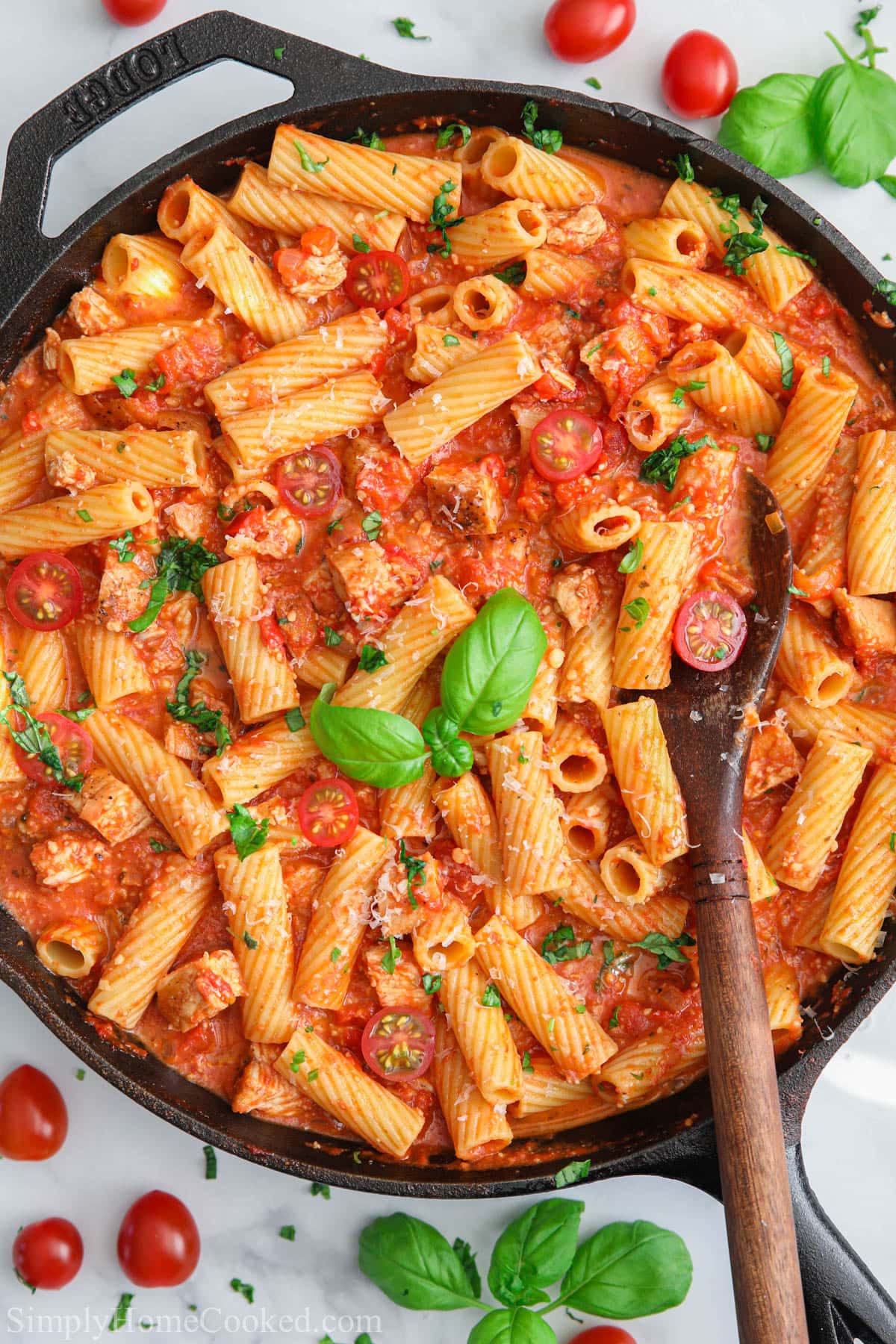 Pan of Chicken Riggies with a wooden spoon and basil.