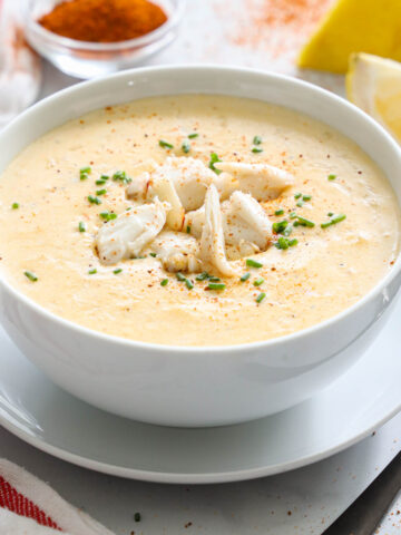 Vertical image of a bowl of She Crab Soup with spices and lemons in the background
