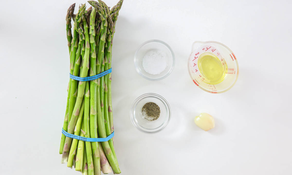 Ingredients for Air Fryer Asparagus, including asparagus spears, avocado oil, salt, pepper, and garlic clove,
