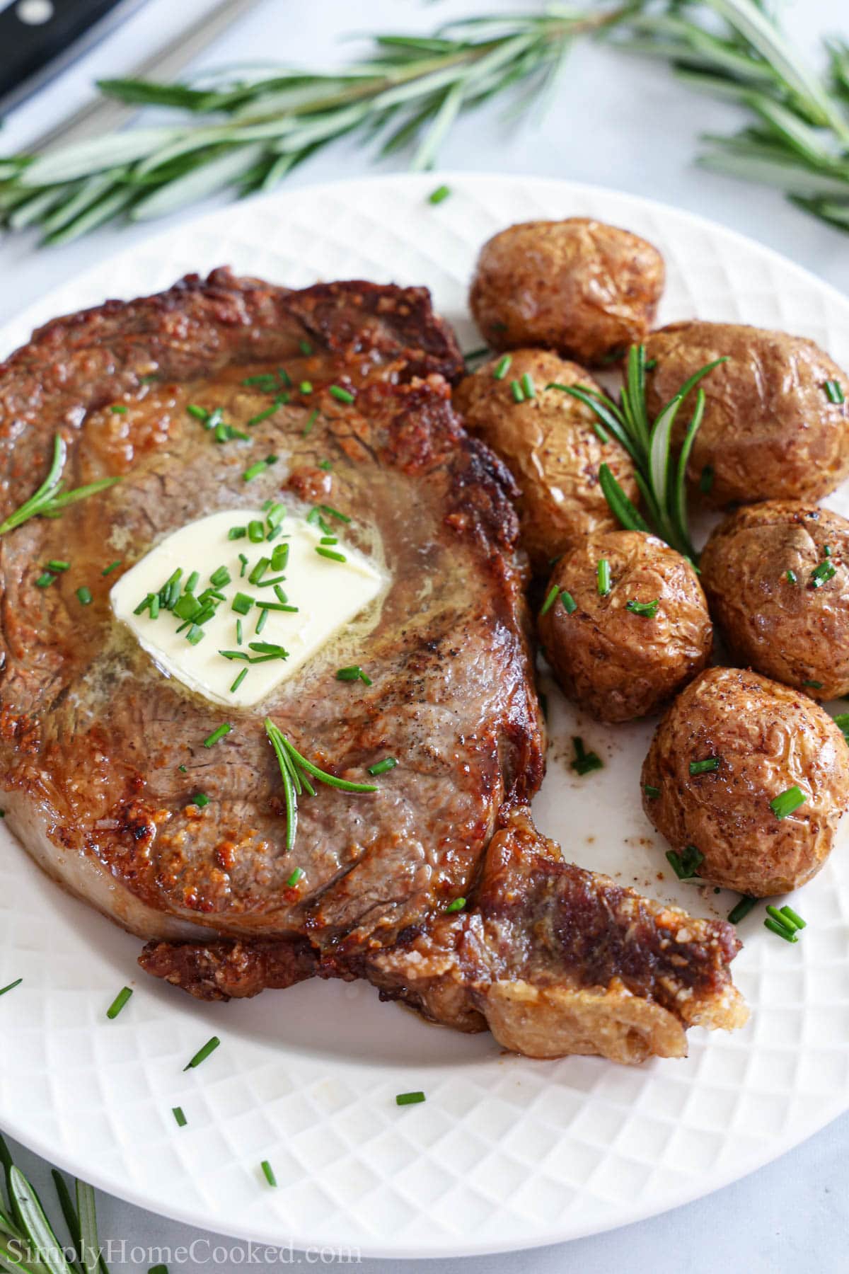Simple and delicious, this Juicy Air Fryer Steak has the perfect crust on the outside and tender meat on the inside. #perfectsteak #ribeyesteak #airfryersteak #juicyairfryersteak Vertical image of Juicy Air Fryer Steak with butter and potatoes on a white plate
