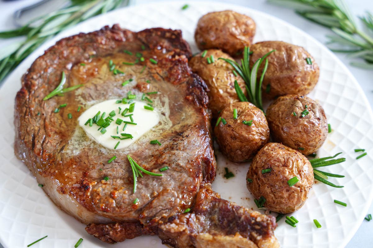 Horizontal image of Juicy Air Fryer Steak with butter and potatoes on a white plate