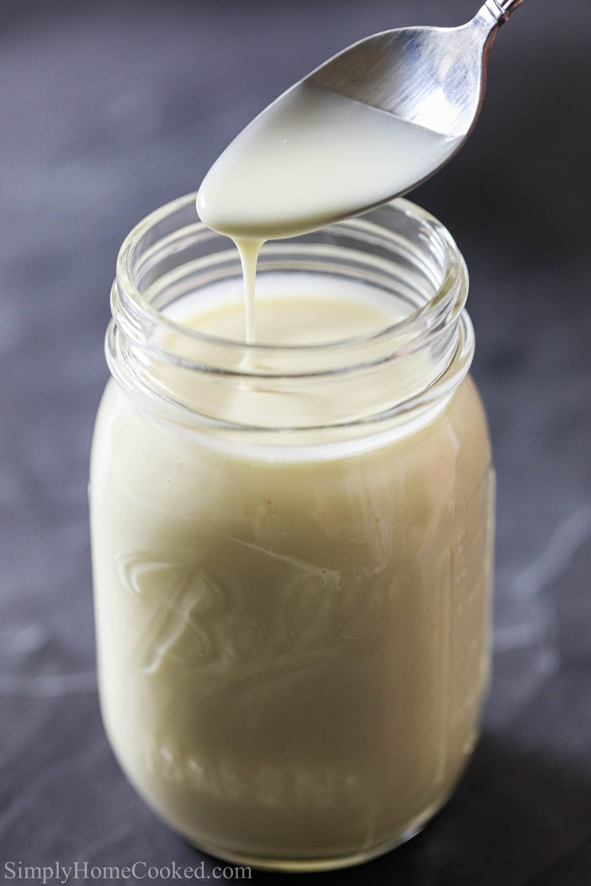 Buttery, rich, and creamy with vanilla and rum flavors, this Vanilla Rum Sauce will make your bread pudding taste absolutely amazing! #rumsauce #rumvanillasauce #dessertsauce #vanillarumdesserttopping Vertical image of Bread Pudding Sauce being drizzled off a spoon into a mason jar.