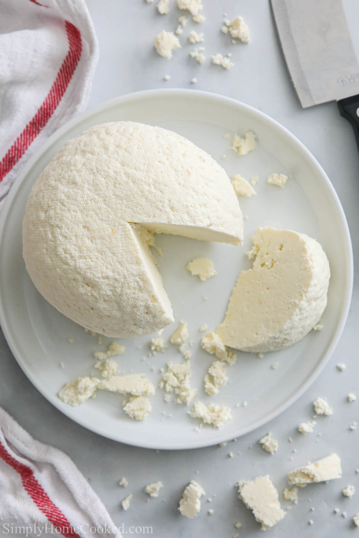 Farmer's Cheese is that creamy treat that you never knew you needed. Follow my simple recipe for this easy to make savory treat. #farmerscheese #tvorog #russianfarmerscheese #homemadecheese #cheesefilling #cheeserecipe Vertical image of a plate of Farmer's Cheese molded with a slice cut out and crumbles nearby