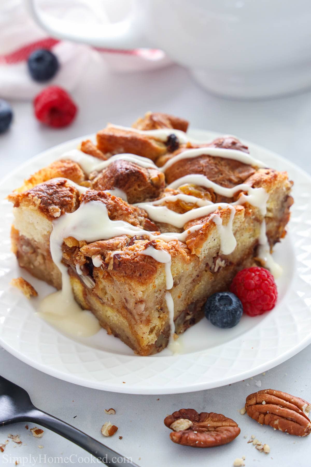 This bread pudding recipe with warm vanilla rum sauce is the perfect dessert for any occasion. Its full of fluffy brioche bread, golden raisins, and pecans. #breadpudding #comfortfood #comfortdessert #bakeddessert #rumsauce #vanillasacue a slice of Bread Pudding covered in vanilla rum sauce on a plate with berries.