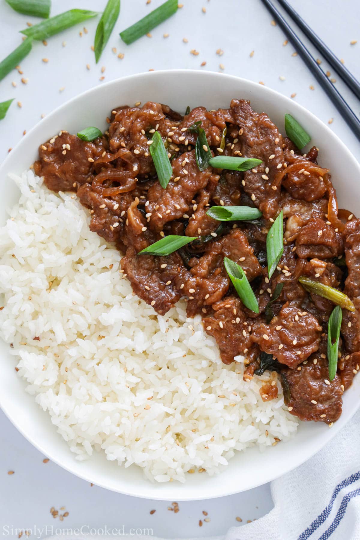 Easy, quick and delicious Mongolian beef recipe. Perfect for a busy weeknight dinner. #mongolianbeef #beefrecipe #asianfood #quickdinner #lowcarb Vertical image of Mongolian Beef with green onions and rice on a white plate