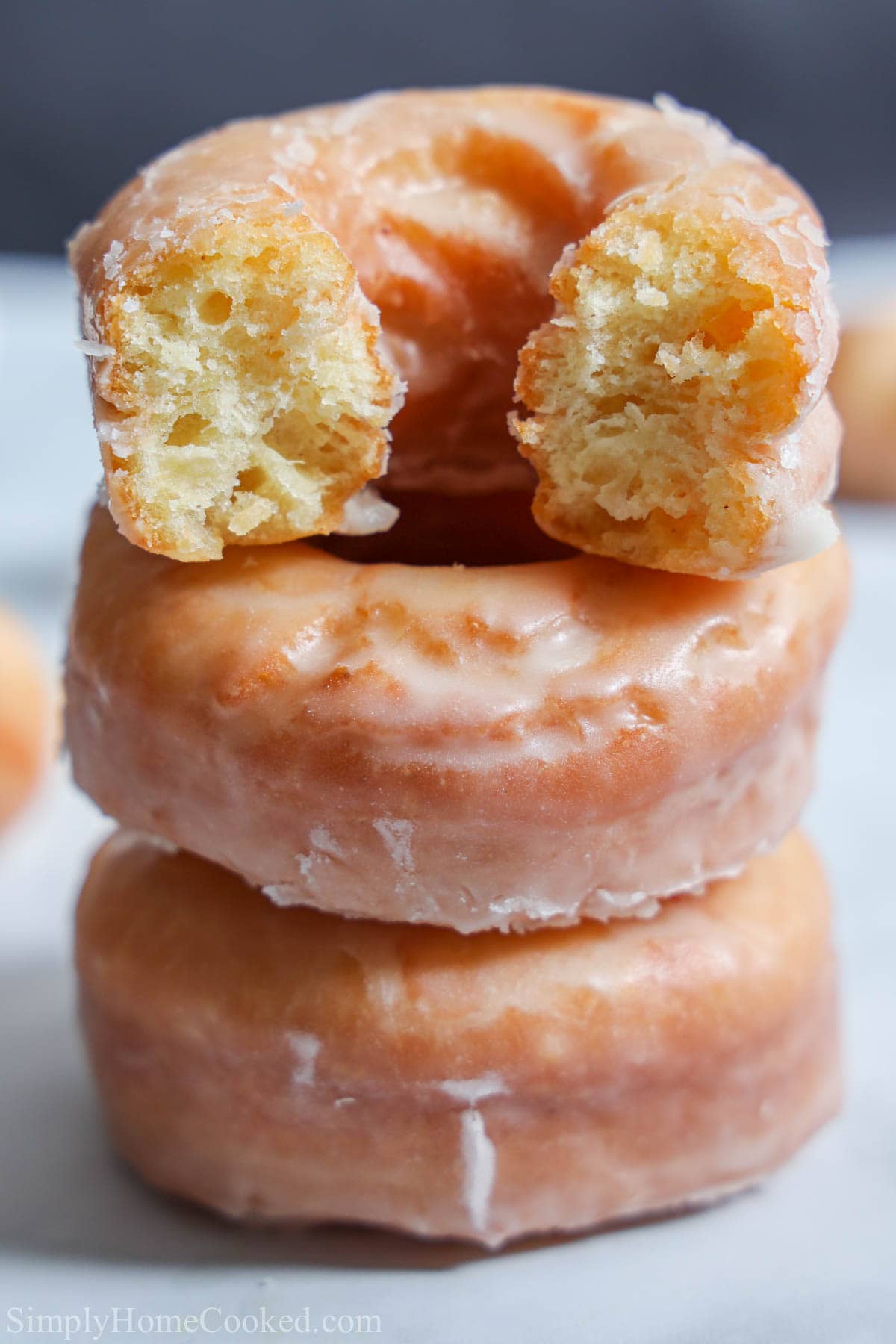 These Old Fashioned Sour Cream Donuts are cakey & moist, with a nice crust. They're dipped in glaze & taste just like at the donut shop. #sourcreamdounuts #oldfashioneddonuts #oldfashionedsourcreamdonuts #oldfashionedsourcreamdonutrecipe Old Fashioned Sour Cream Donuts in a stack with the top one missing a bite.