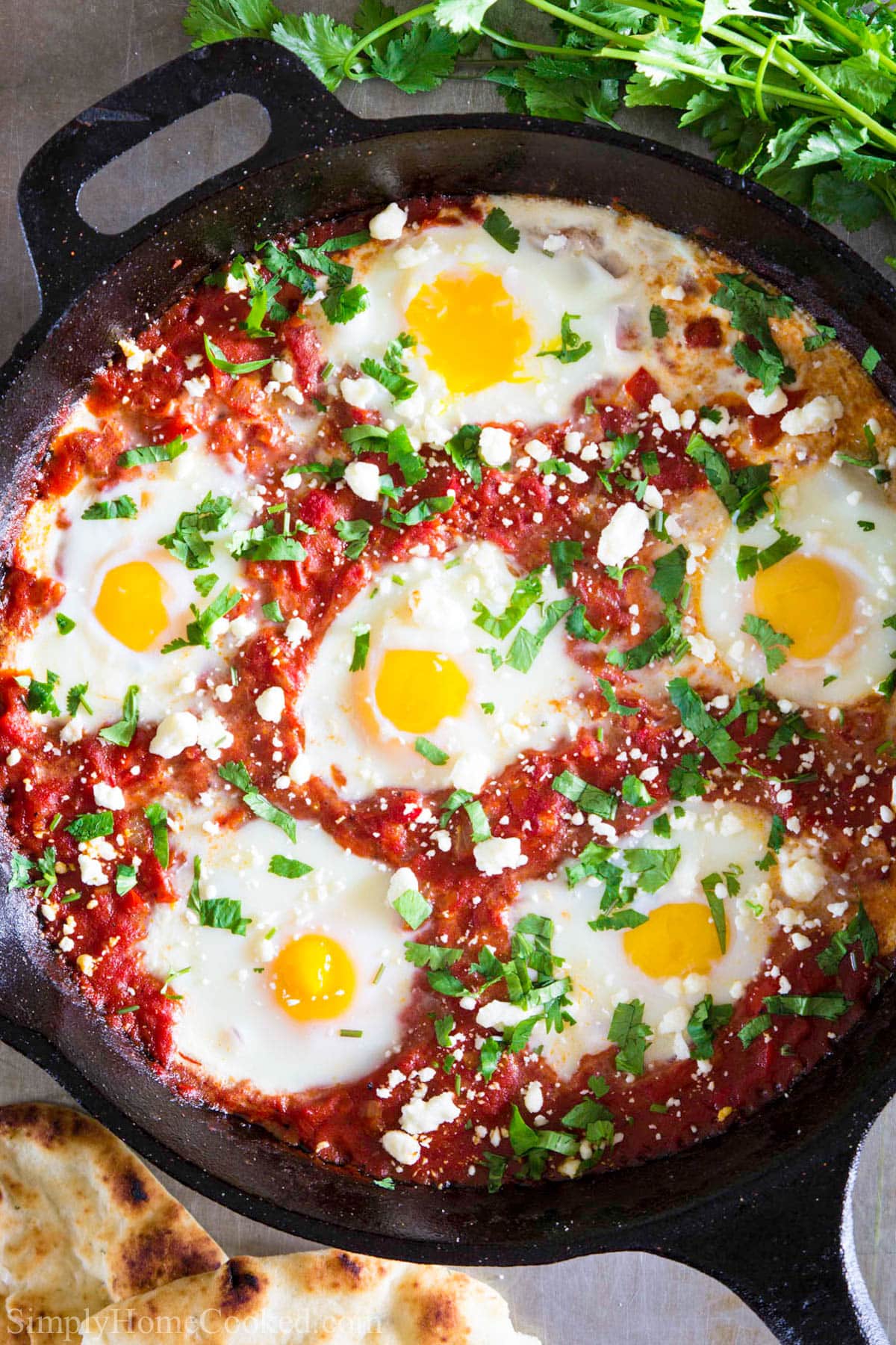 Shakshuka is a flavorful Middle Eastern recipe that is easy to make & tastes delicious. Whether you eat it for breakfast or dinner, you'll love this egg dish.. #middleeasternfood #israelifood #breakfastdish #easyshakshukarecipe Shakshuka in a cast iron pan topped with feta cheese and cilantro.