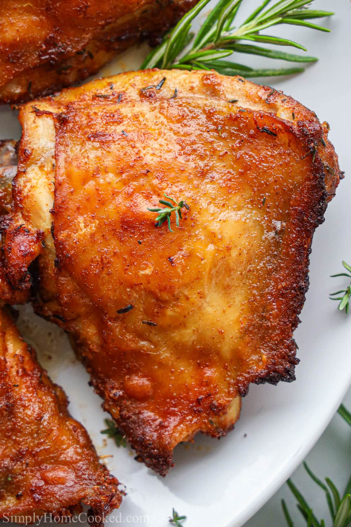 Close up of Air Fryer Chicken Thighs on a white plate with rosemary sprigs. 