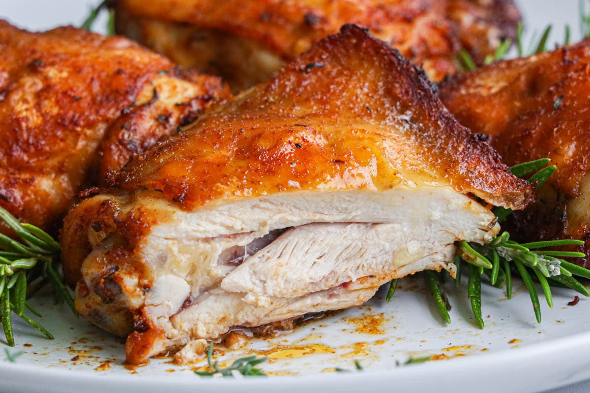 Horizontal image of Air Fryer Chicken Thighs on a white plate with rosemary sprigs, one thigh sliced.
