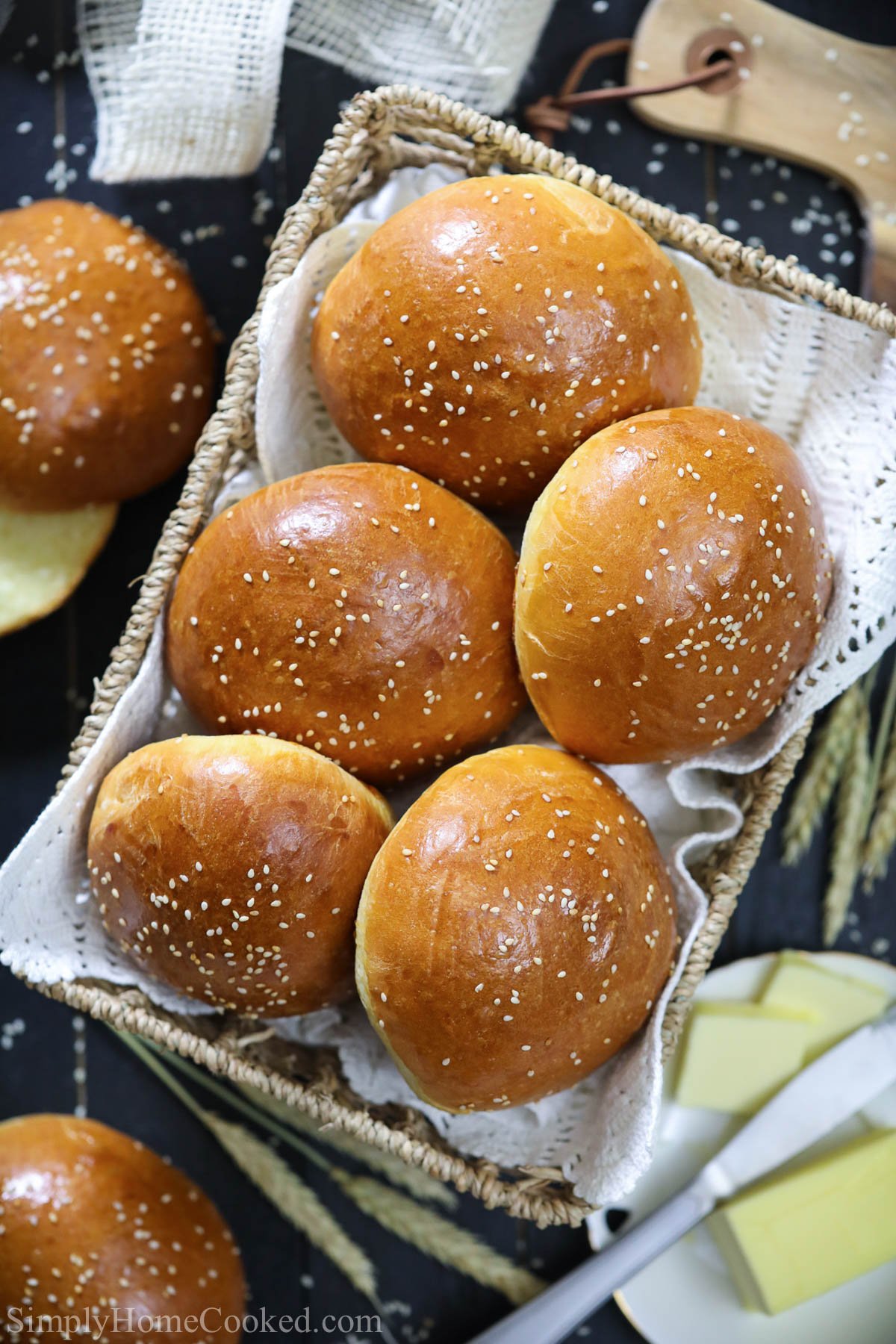 Overhead vertical image of Brioche Buns topped with sesame seeds in a basket, with butter nearby
